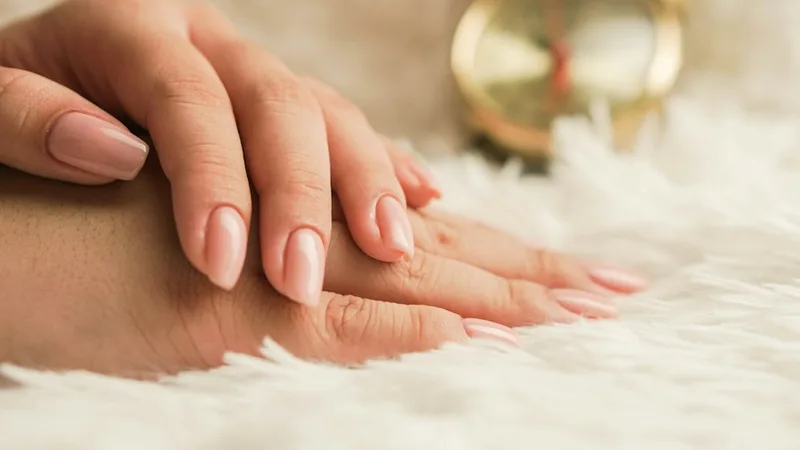 A soft nude manicure resting on a light textured surface